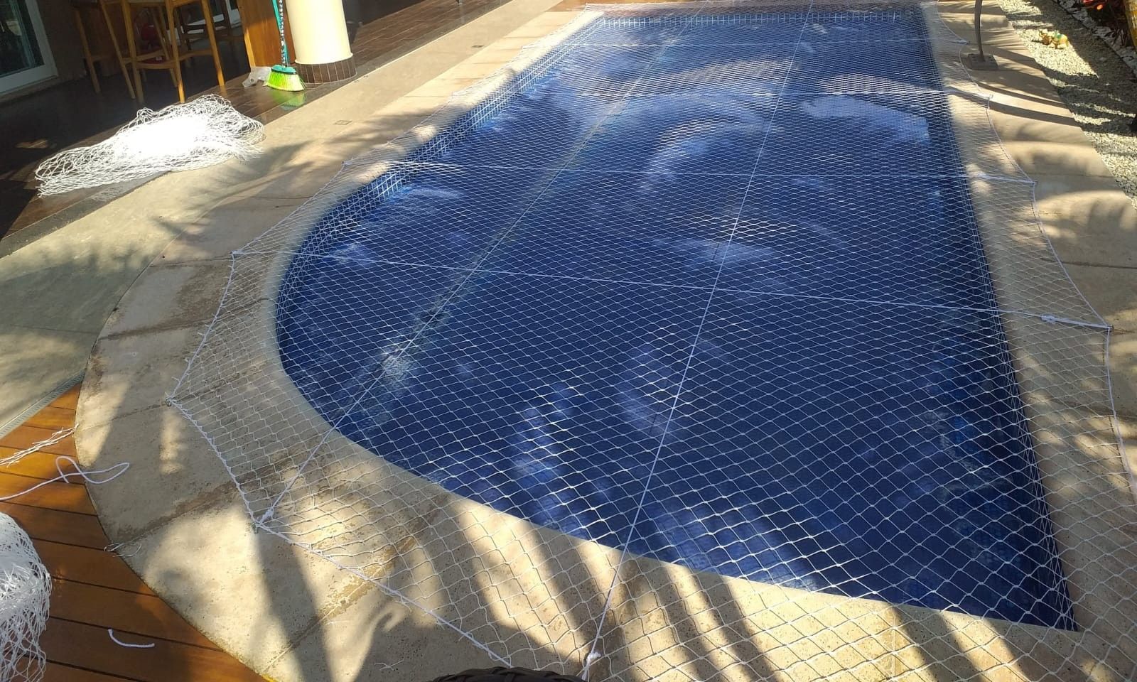 Piscina coberta por rede de proteção, tensionada sobre a água e presa ao deck