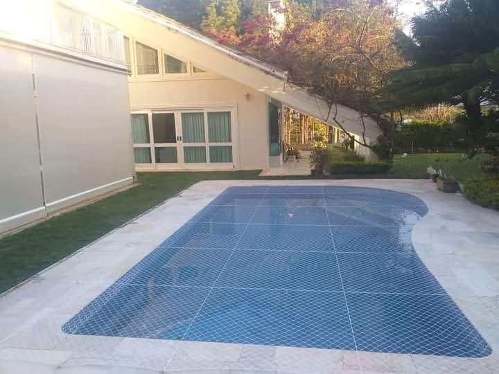 Piscina de casa coberta por rede de proteção, com jardim ao lado