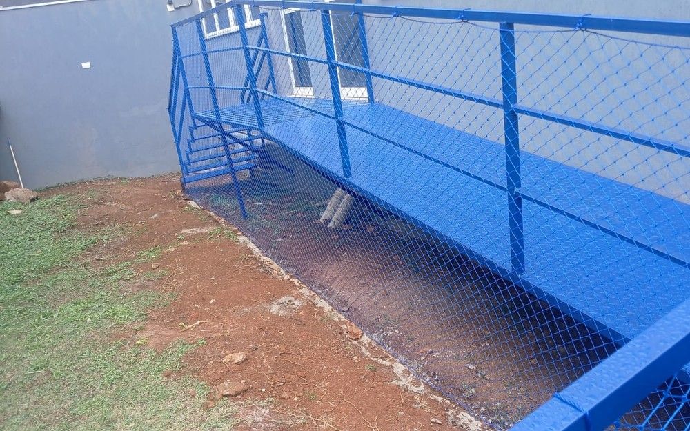 Rampa externa com guarda-corpo azul protegido por rede de proteção azul