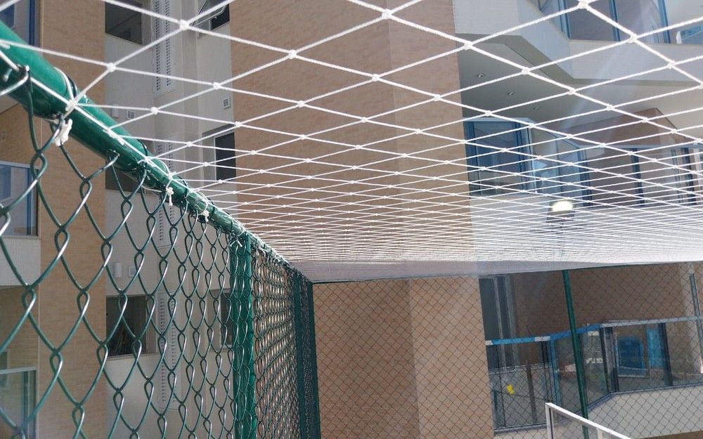 Rede de proteção branca instalada como teto sobre quadra de condomínio