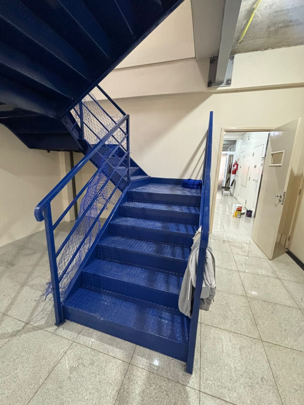 Lance de escada metálica azul com rede de proteção no guarda-corpo lateral