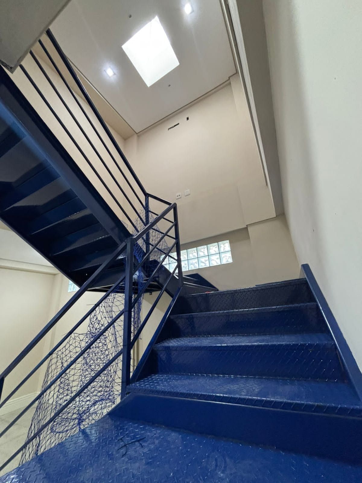 Escada metálica azul com rede de proteção azul fechando o vão do guarda-corpo