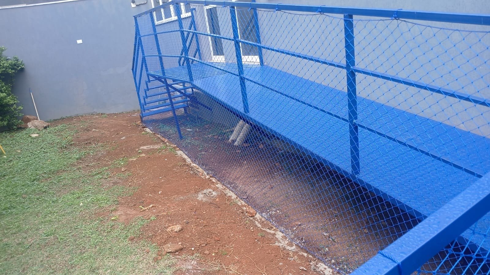 Rampa externa com guarda-corpo azul protegido por rede de proteção azul