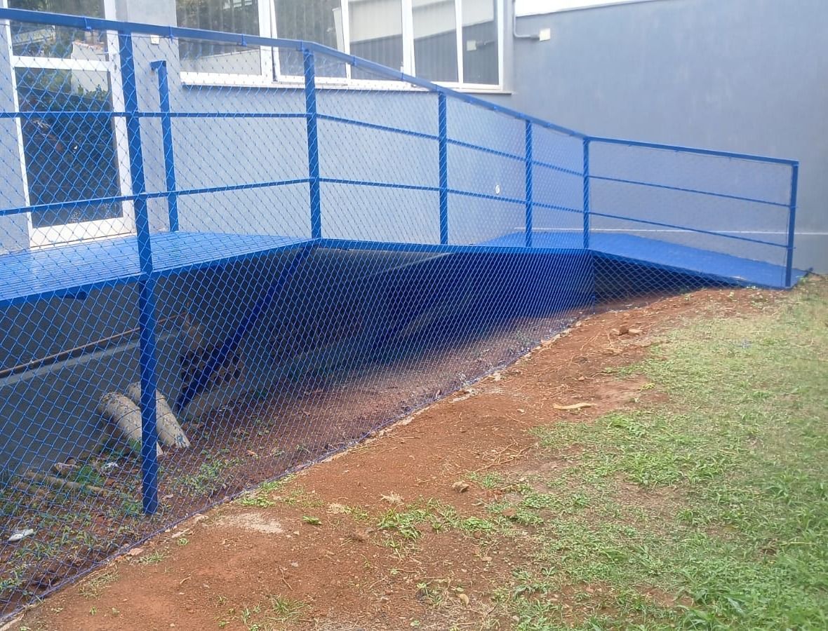 Rampa externa com guarda-corpo azul fechado por rede de proteção azul